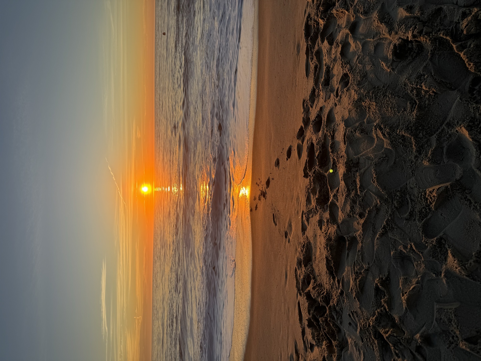 Atardecer en la playa con huellas en la arena hacia el sol — foto real